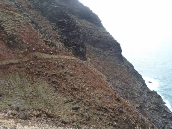 A Ana, Laura e Rafa caminham por trilha na beira de um penhasco, a caminho da Kalalao Beach, na Na'Pali Coast, em Kauai, no Havaí